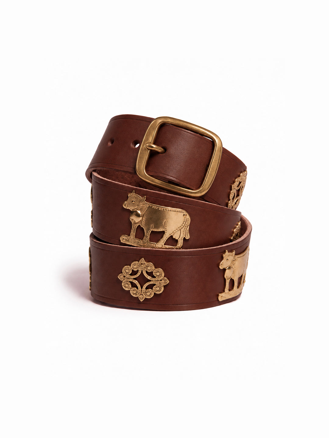 A brown leather belt with antique gold-toned metal accents, including cow figures and decorative medallions, coiled on a white background. The Alpine Belt, Appenzeller belt, made in Switzerland, handmade, mountain belt, leather belt, cintura di pelle, cintura con le mucche, stelle alpine, cintura svizzera, cintura tirolese, cintura ampezzana, traditional belt, cow belt, kids belt, artisanal kids belt, artisanal belt, cinture da bambini, cinture artigianali.